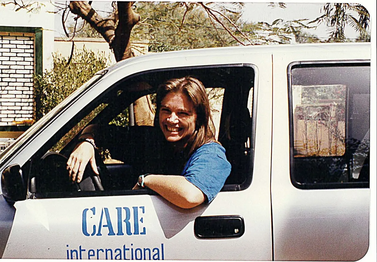 A young woman with brown hair leans out the window of a white pickup truck marked “CARE International.”