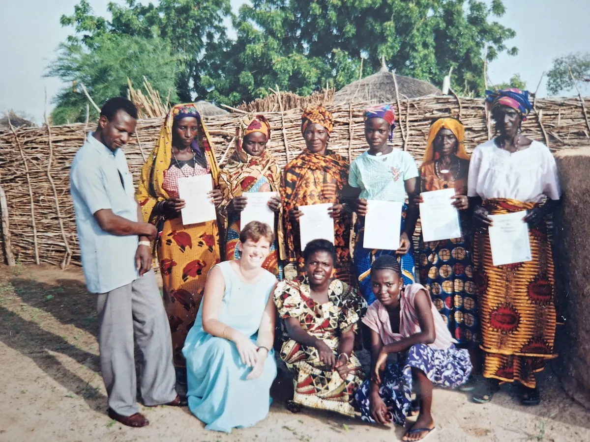 A group stands in front of a woven fence, several women holding certificates, with Moira and two colleagues kneeling in front.