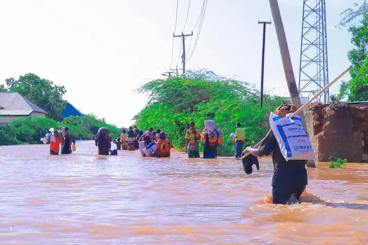 A wideshot of a group of people walking through floodwaters that come up to their knees.