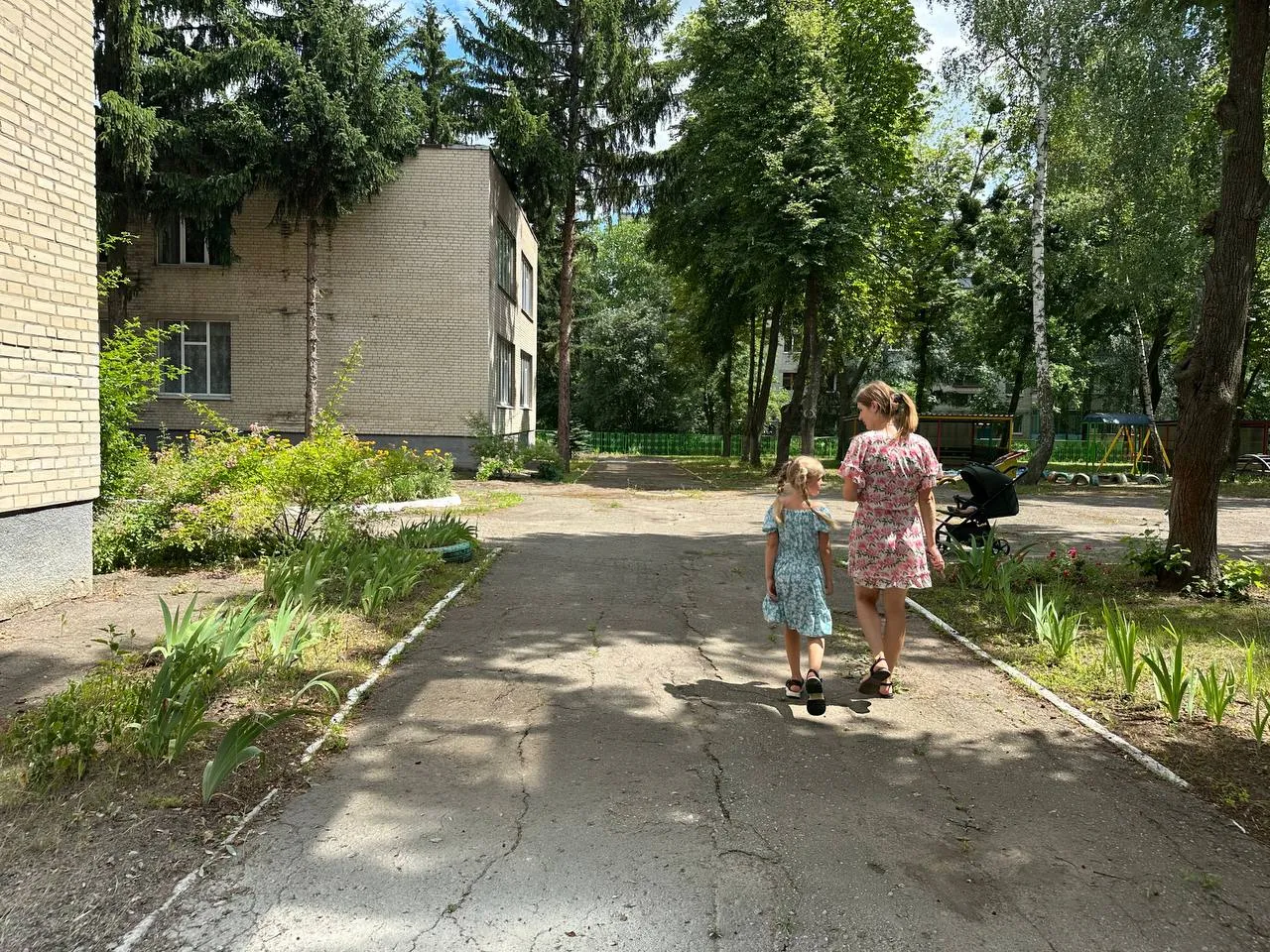 Mother and daughter walking near park on a sunny day.