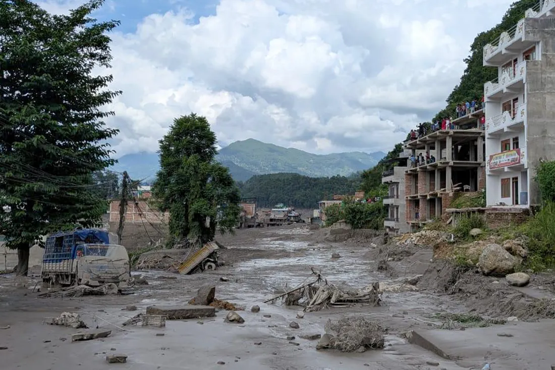 The impacts of flash flooding in Nepal, showing a devastated building and debris in a muddy street.