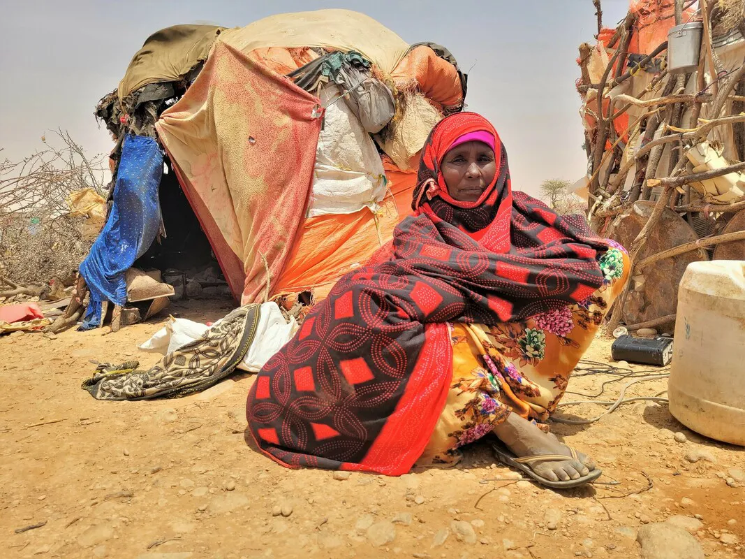 A Somalian woman sits outside a tent covered in colorful fabrics.