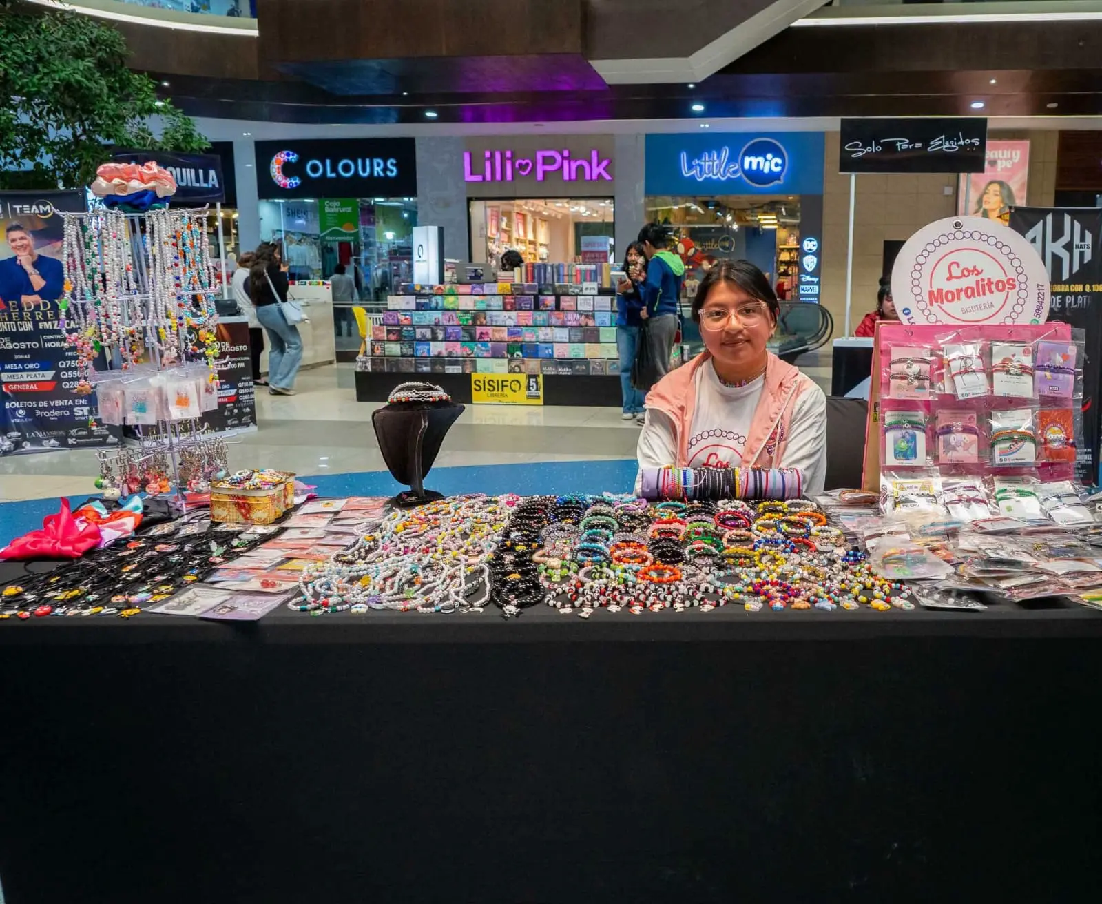 A young woman is sitting at a table covered in handcrafted jewelry.
