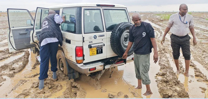 Three CARE Sudan staff members work to free a mud-stuck 4x4 vehicle on an impassable road during the Sudan humanitarian crisis in South Kordofan.