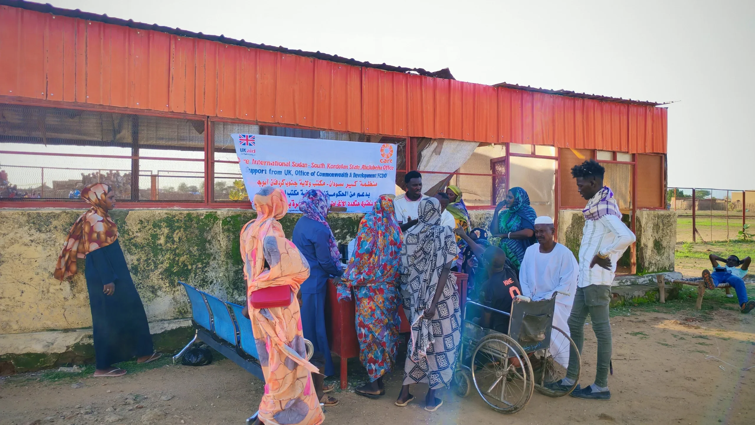 A diverse group of community members, including a man using a wheelchair, gather to register for multipurpose cash assistance at the CARE office in Abu Jubayhah, South Kordofan.