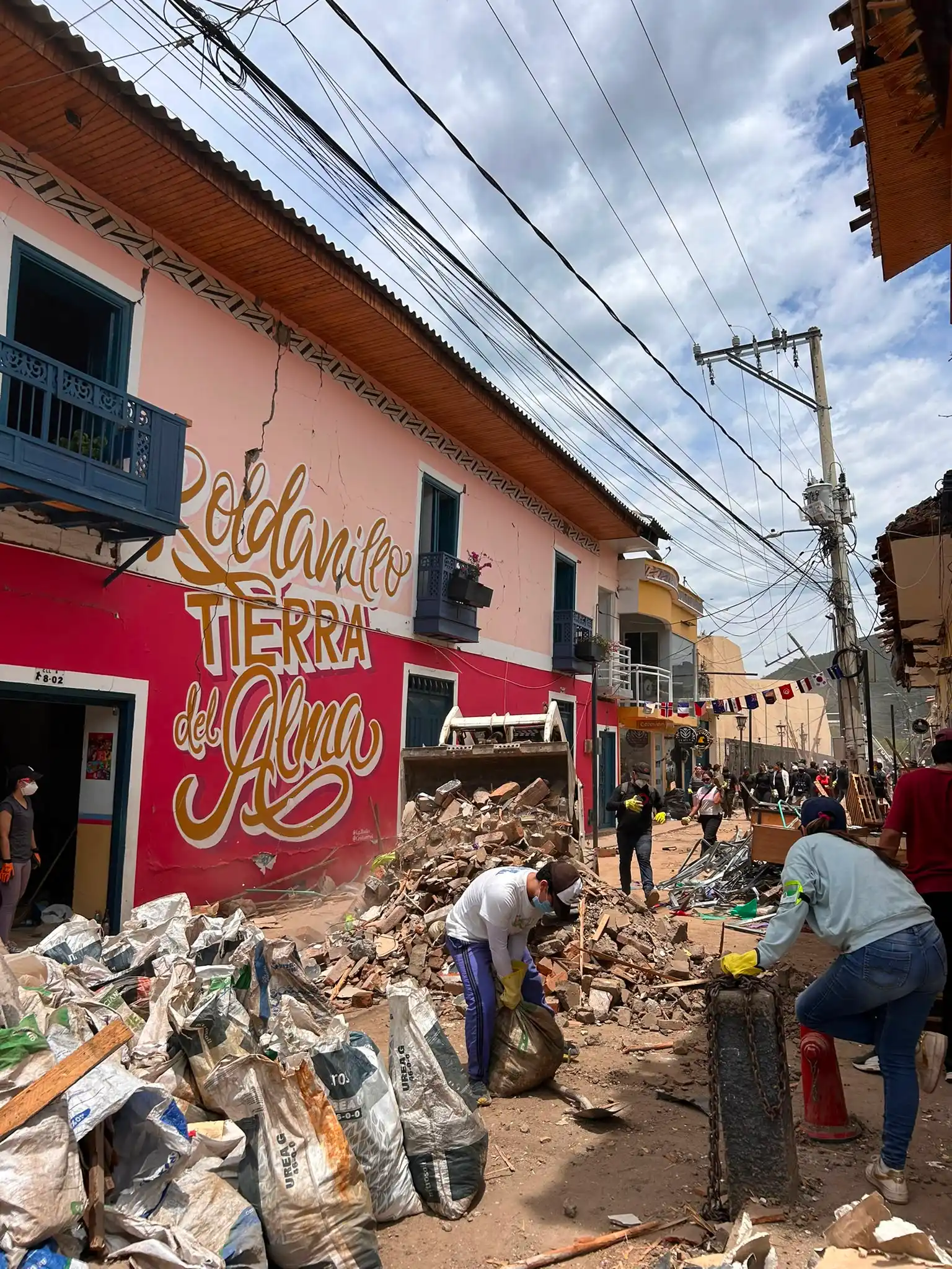 Volunteers and heavy machinery clean up rubble and fill debris bags on a street in Roldanillo following the Colombia earthquake.