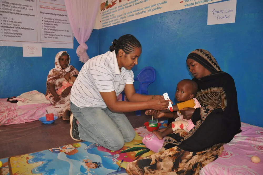 A nurse examines a young child during malnutrition treatment.