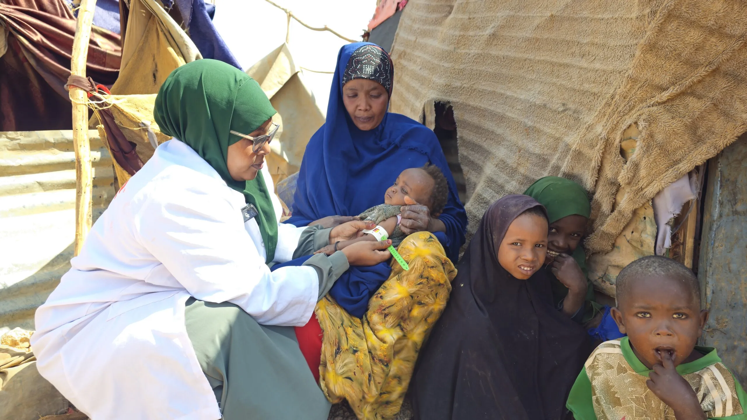 A health worker examines a baby while a mother and other children sit nearby.