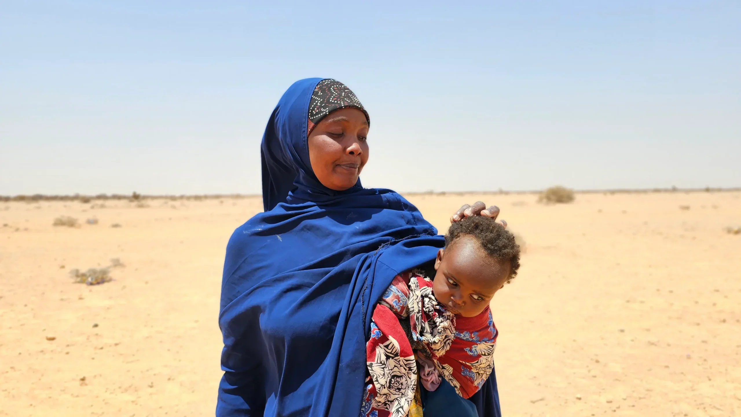 A mother holding her baby in the desert on a sunny day.