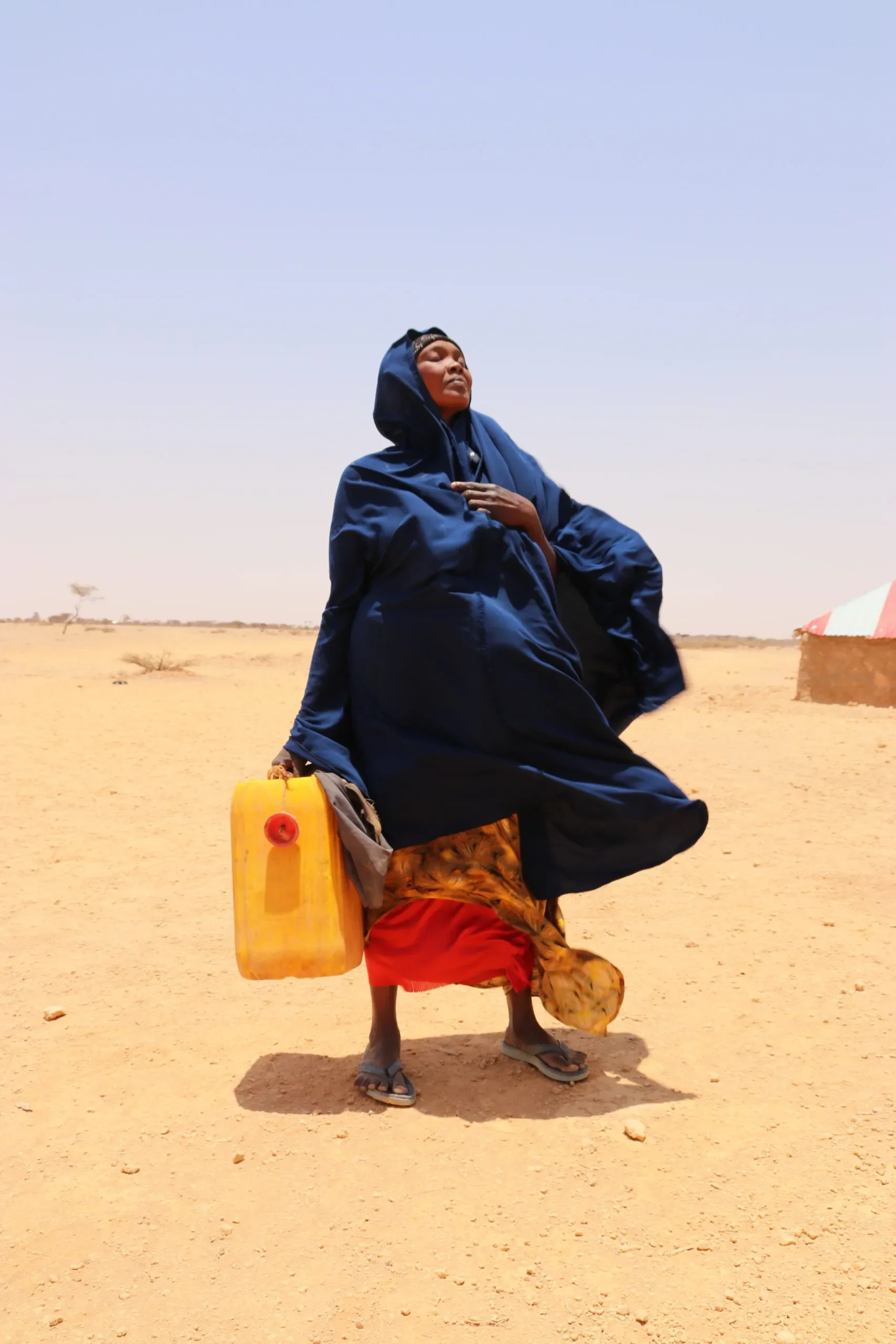 Woman standing in the desert holding an empty yellow water container.
