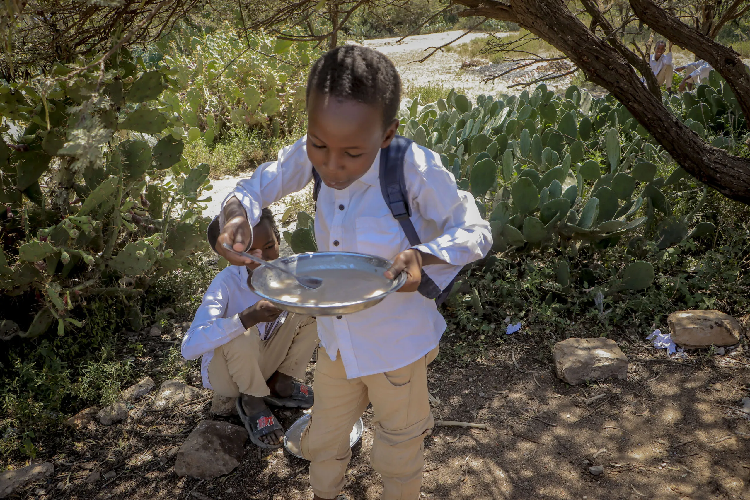 A child eating lunch from a bowl outside of school.