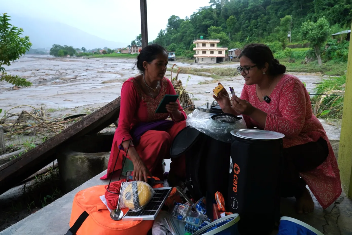 Two women compare small household items — a lighter and toothpaste — pulled from a CARE PACKAGE for Emergencies kit. 