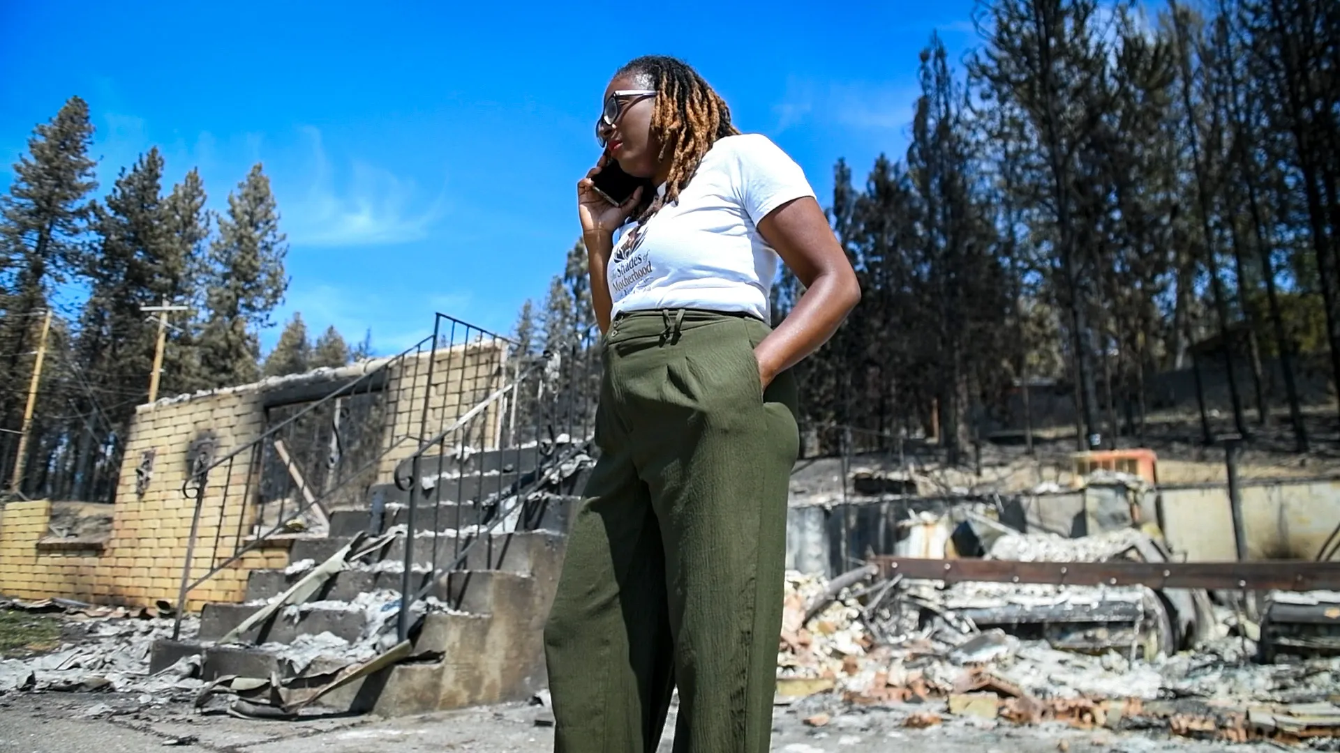 A woman talking on a cell phone in front of remnants of burnt down house.