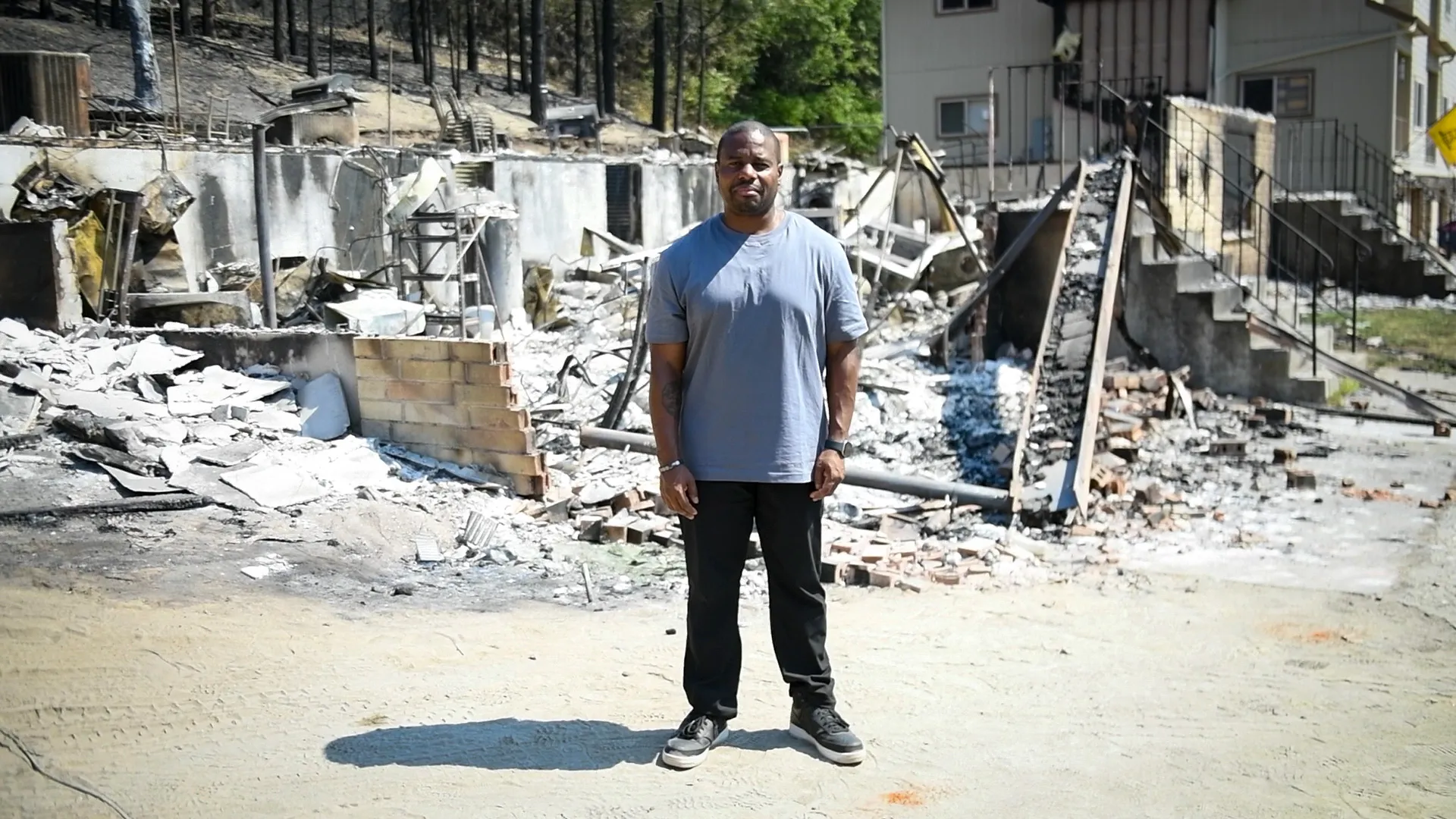 A man standing in front the burnt down remnants of his home.
