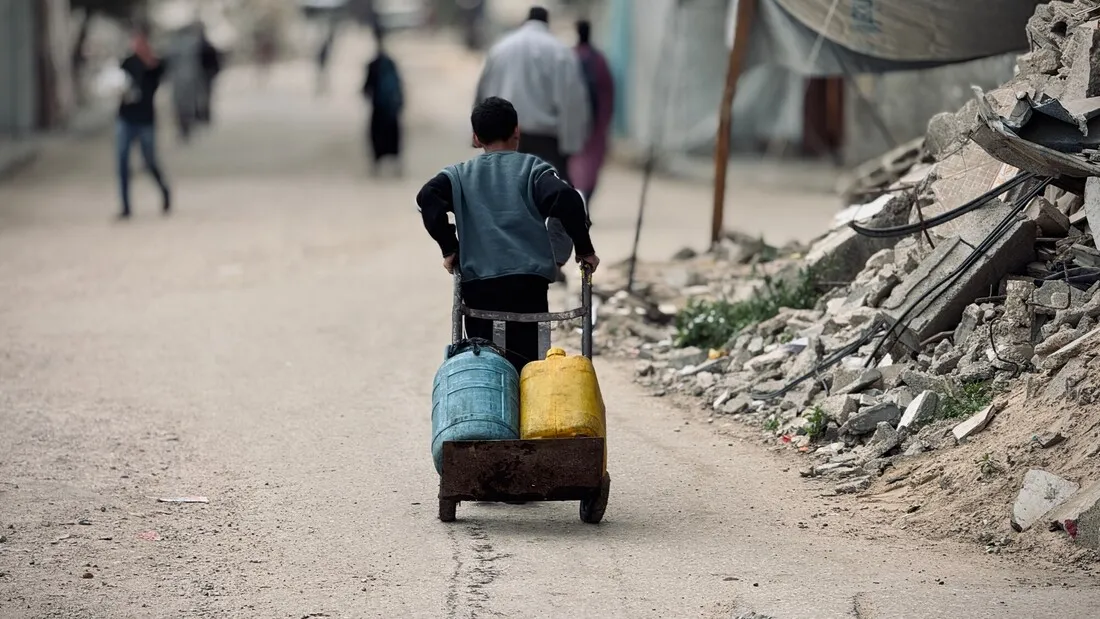 An image of a young boy carrying two jerrycans on a cart.