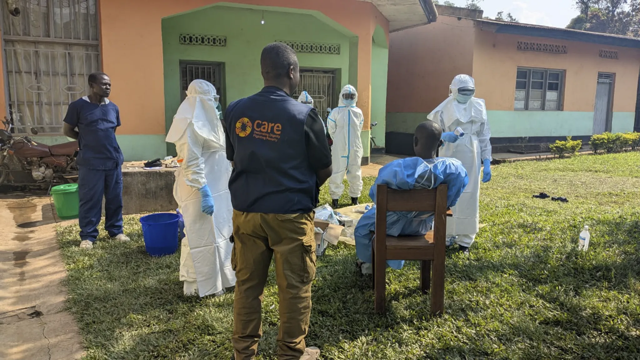 CARE health workers in hazmat outfits participate in a training exercise outside a health center with a person pretending to be a patient.