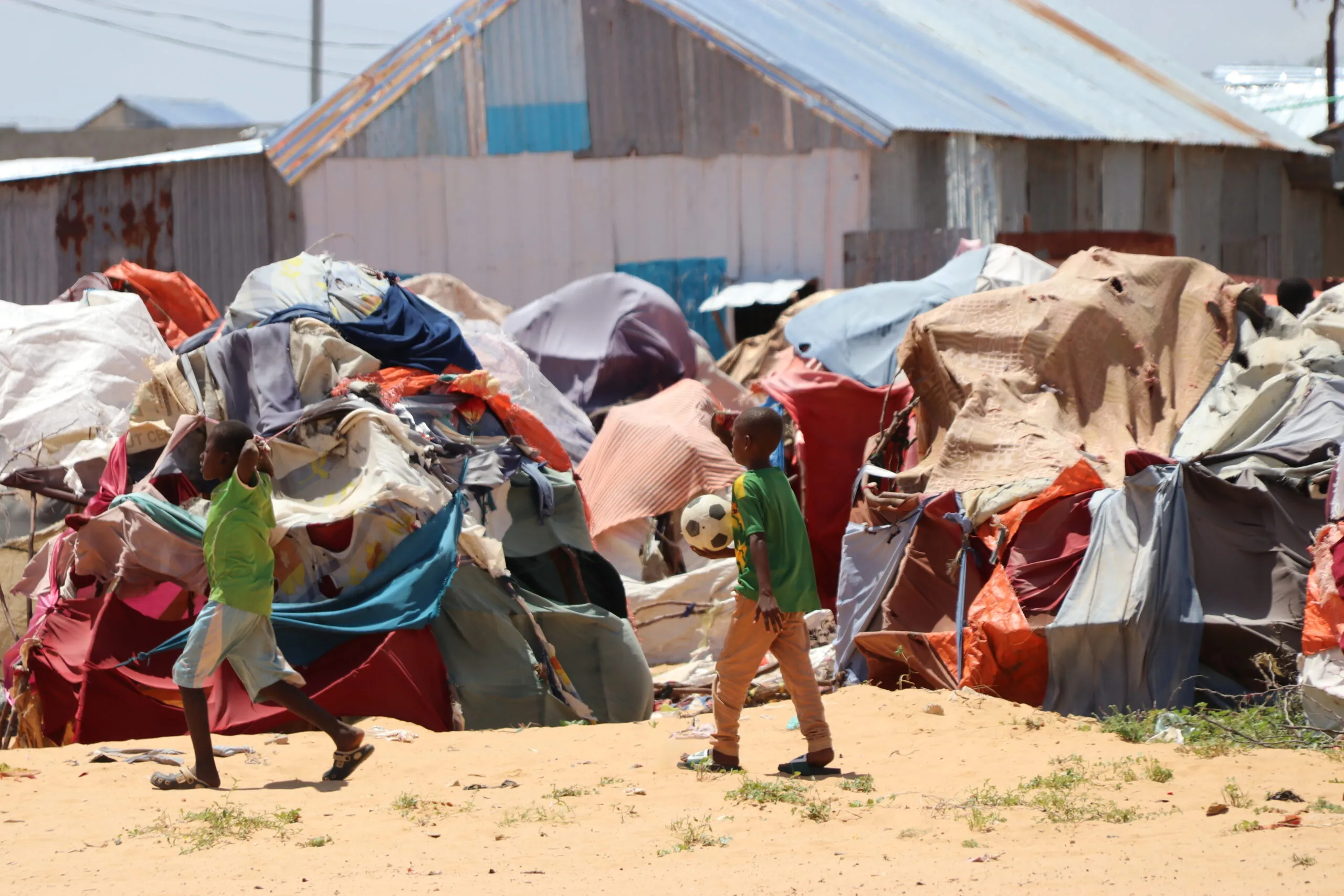 Two children walk between tightly packed makeshift shelters covered with tarps and fabric in a displacement camp in Mogadishu.